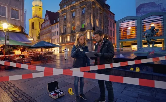 TabCrime Academy in Dortmund: Zwei Ermittelnde mit Spurenkoffer hinter rot-weißem Absperrband auf einem Dortmunder Platz.
